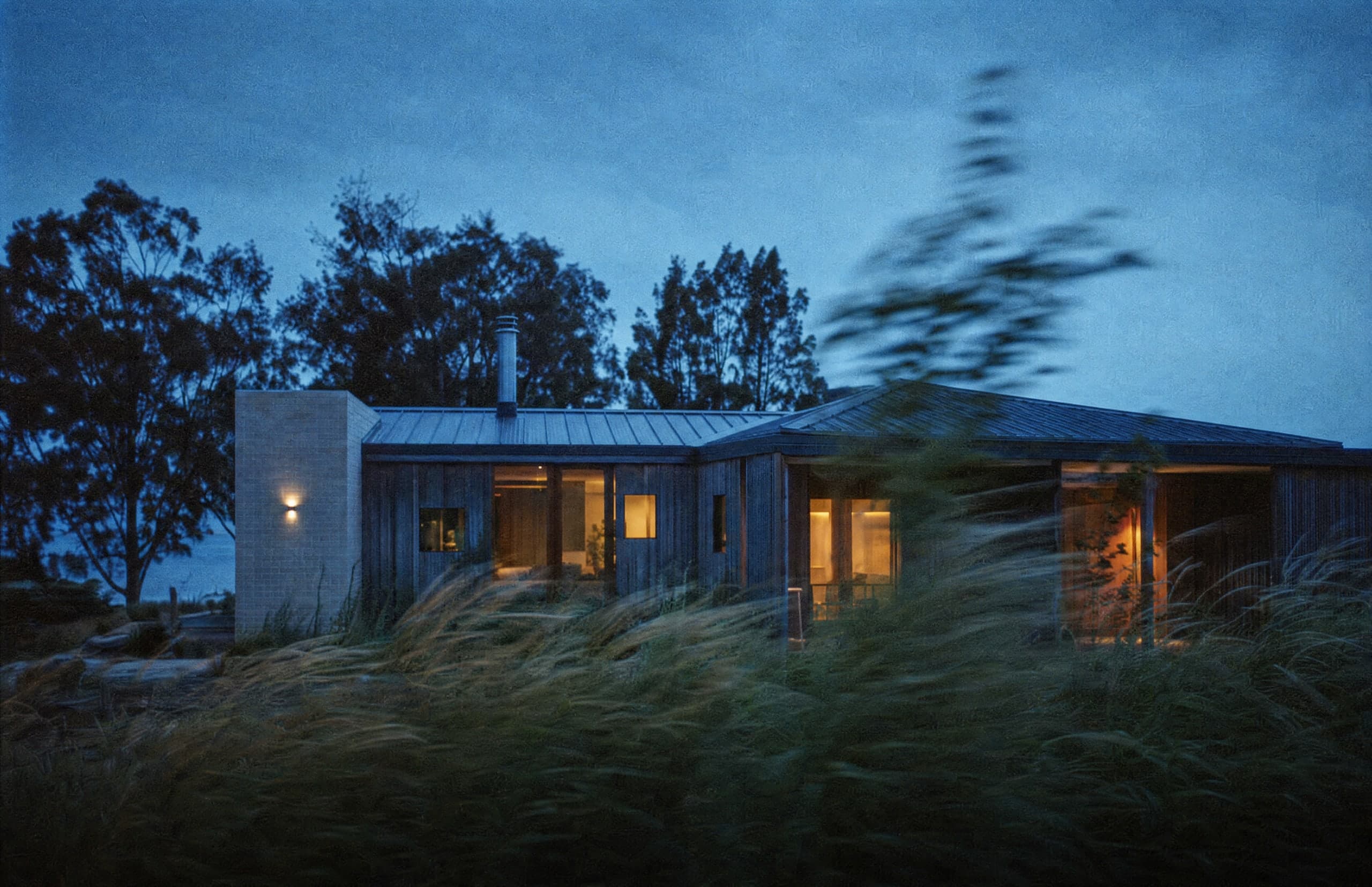 An architect-designed timber home with warm windows in the evening landscape.