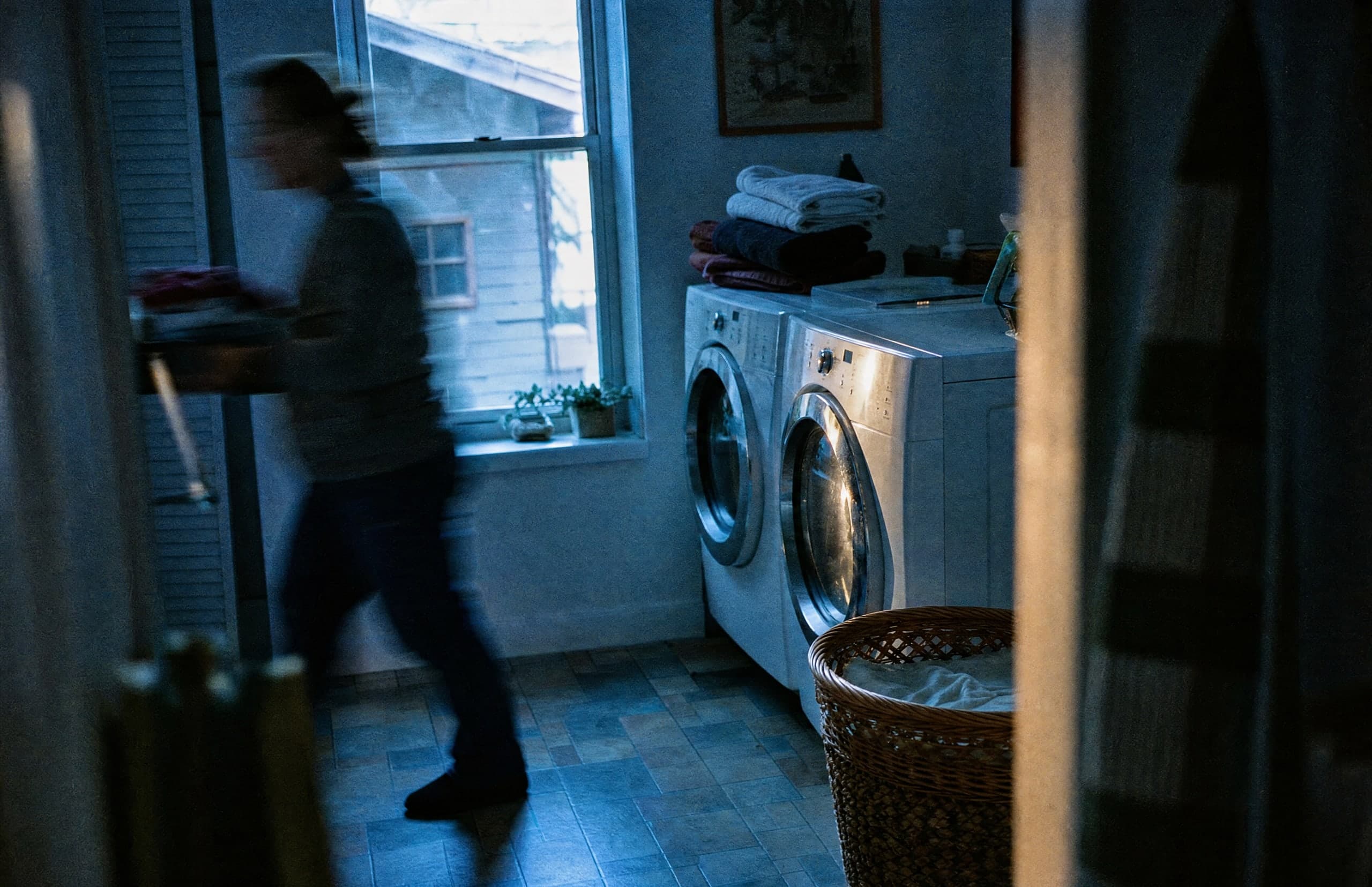 A pair of laundry appliances in a lived-in home, with someone carrying laundry through the room.