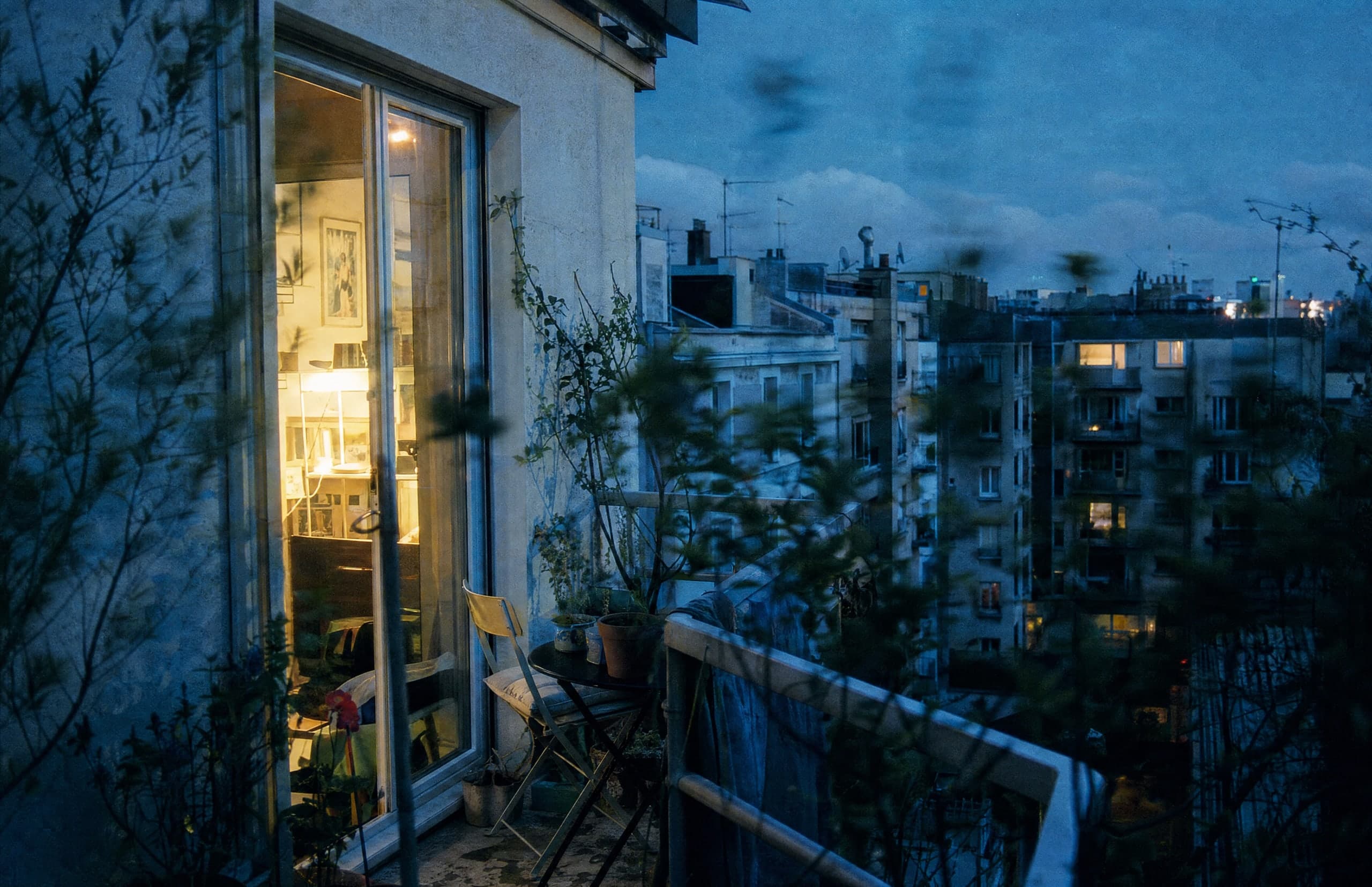 A warmly lit apartment opening onto a planted balcony at dusk.