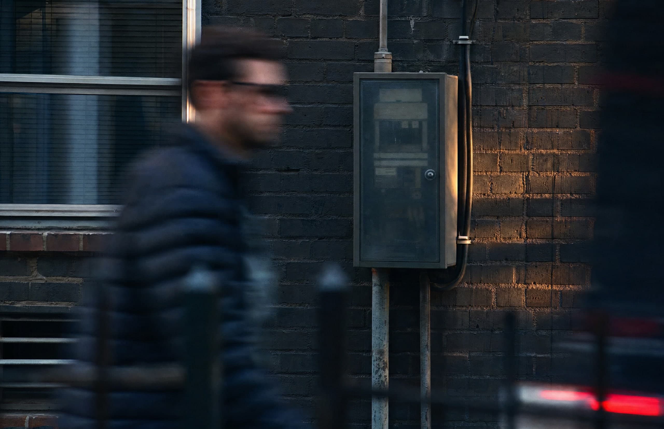 An exterior electrical switchboard on a brick house, with a person passing in the foreground.